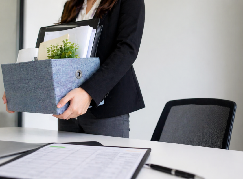 Employee in a tan blazer packs up her desk and prepares to leave.