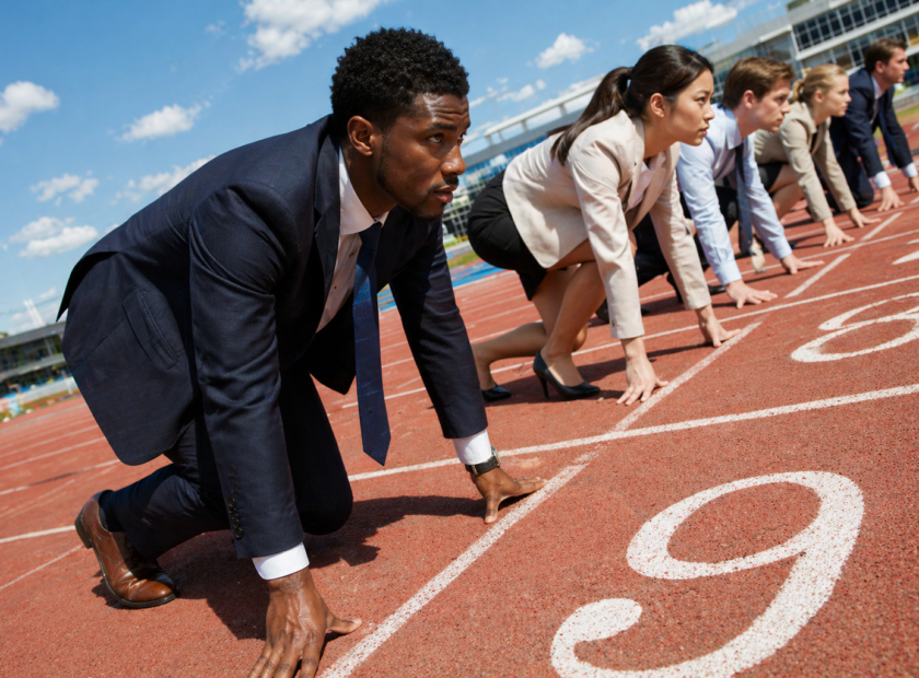 People in business wear line up in sprinter blocks on a racing track.