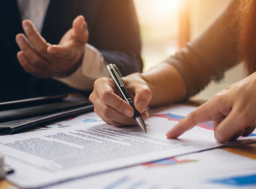 Hands point to a contract as one person prepares to sign.
