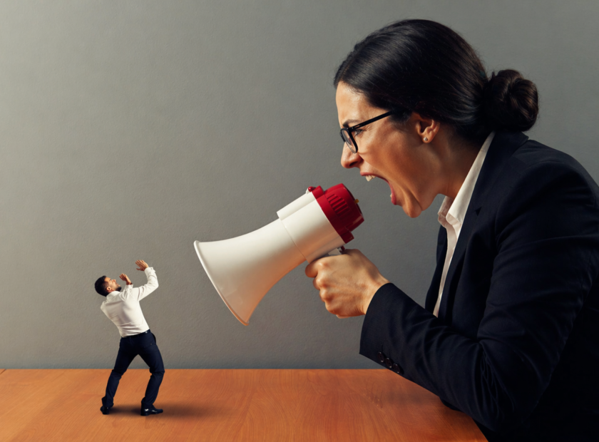 Bad female executive coach with megaphone yells at miniaturized employee on desk