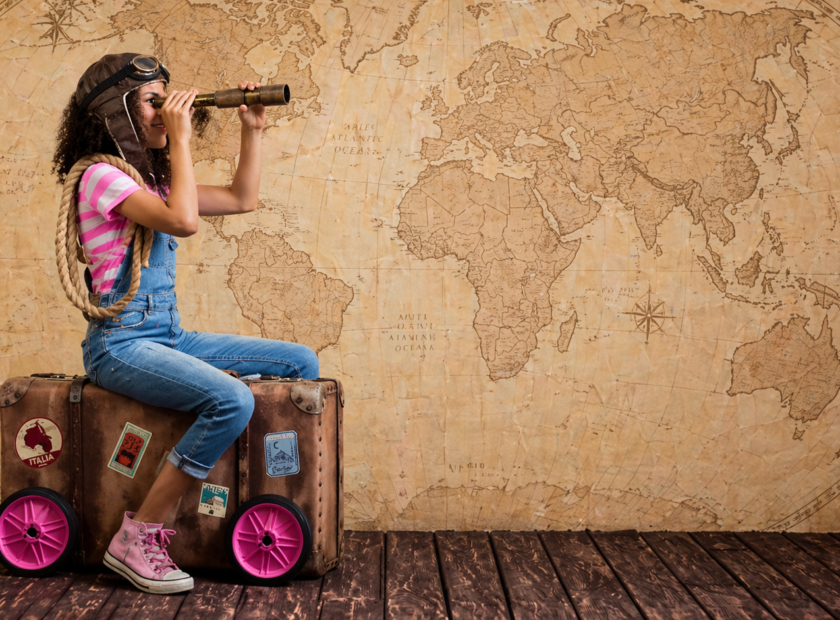 Child holds monocular while sitting on luggage, pretending to be a sailor.