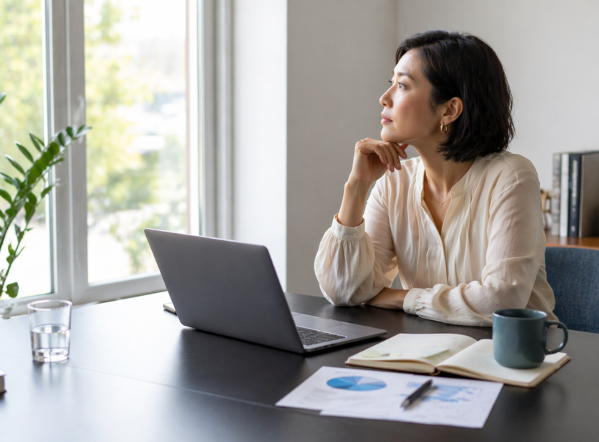 Executive woman sits at a conference desk and looks out the window while pondering future decisions.