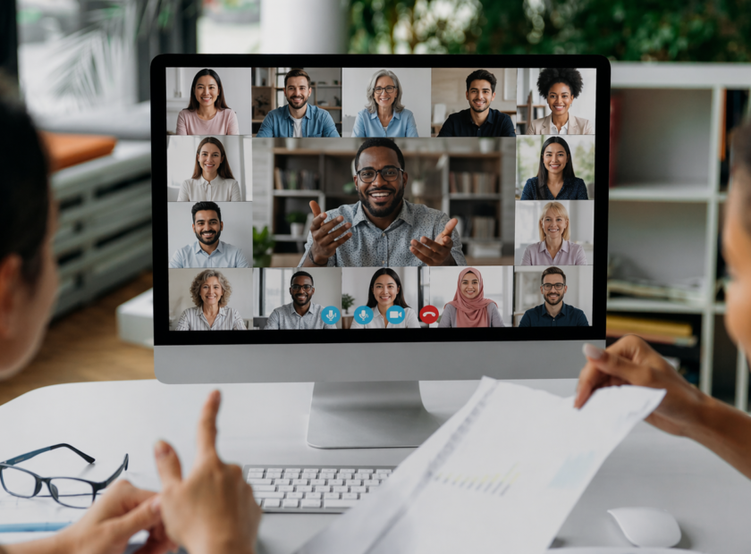 Two women sit in front of a computer monitor during a large group video chat session.