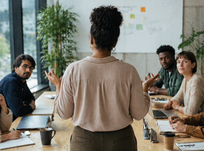 Standing woman speaks in front of team in a board room.