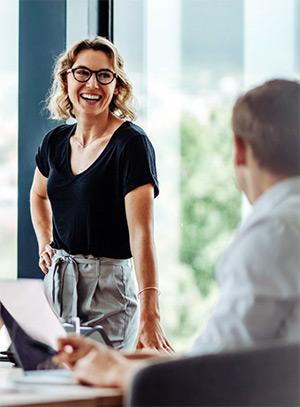 Woman and man in office talk as woman stands and smiles.