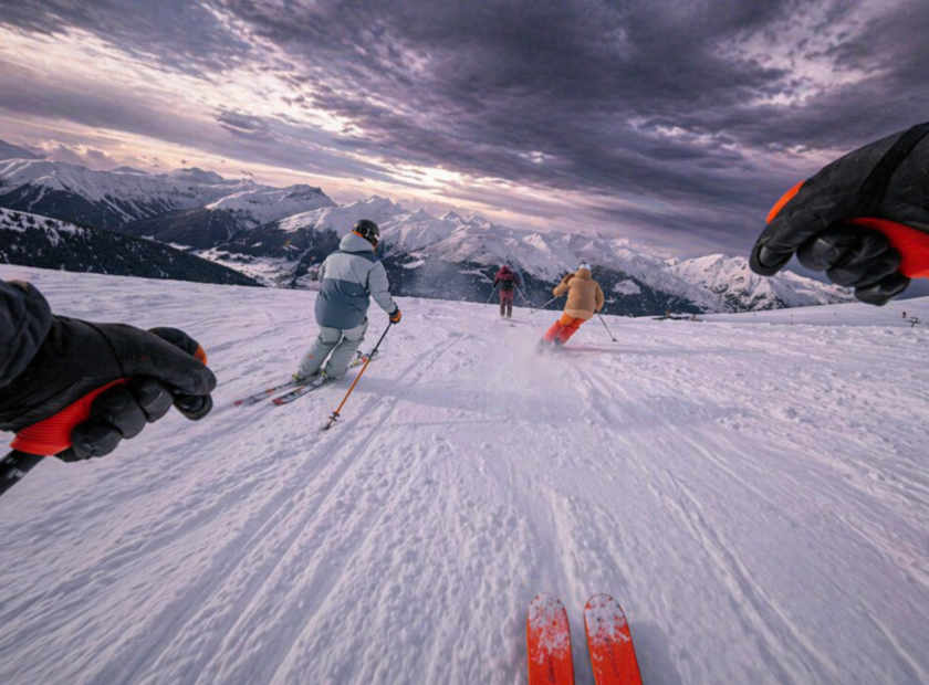 Skiier with orange skis goes down mountain with other skiiers in front.