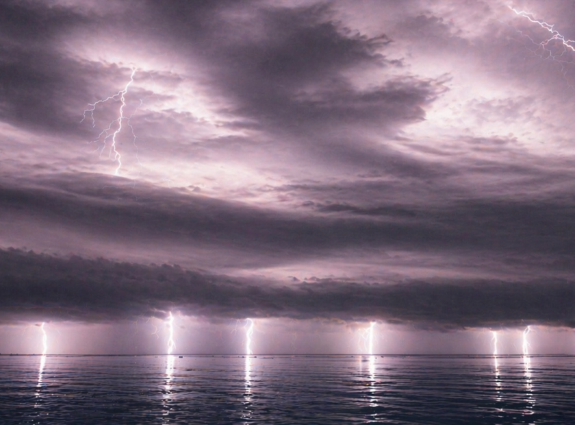 Multiple lighting bolts light up an ocean at night.